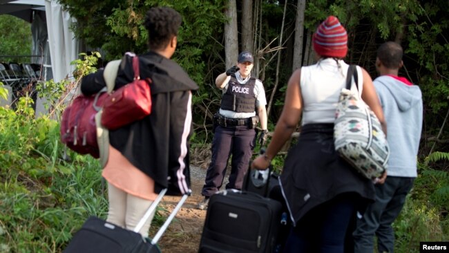 FILE - A Royal Canadian Mounted Police (RCMP) officer watches as a family from Haiti arrive to cross the U.S.-Canada border into Canada from Roxham Road in Champlain, New York, August 11, 2017.