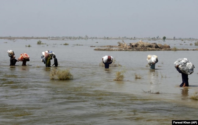 FILE - Victims of heavy flooding carry relief aid in Sindh Province, Pakistan, Sept. 9, 2022.