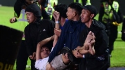 Sekelompok pria tampak membopong salah satu rekannya setelah kekisruhan meletus selepas pertandingan sepak bola antara Arema dan Persebaya di stadion Kanjuruhan, Malang, pada 1 Oktober 2022. (Foto: AFP)