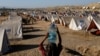 FILE - A girl carries a bottle of water she filled from nearby standing floodwaters at a camp for those displaced by recent flooding, in Sehwan, Pakistan, Sept. 30, 2022. 