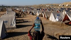 Seorang anak perempuan membawa galon berisi air minum ke area kamp pengungsi yang terdampak oleh banjir di Sehwan, Pakistan, pada 30 September 2022. (Foto: Reuters/Akhtar Soomro)