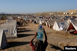 A girl carries a bottle of water she filled from nearby standing flood-waters at a camp for those displaced by recent flooding, in Sehwan, Pakistan, Sept. 30, 2022. (REUTERS/Akhtar Soomro)