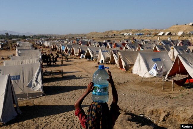 A girl carries a bottle of water she filled from nearby standing flood-waters at a camp for those displaced by recent flooding, in Sehwan, Pakistan, Sept. 30, 2022. (REUTERS/Akhtar Soomro)