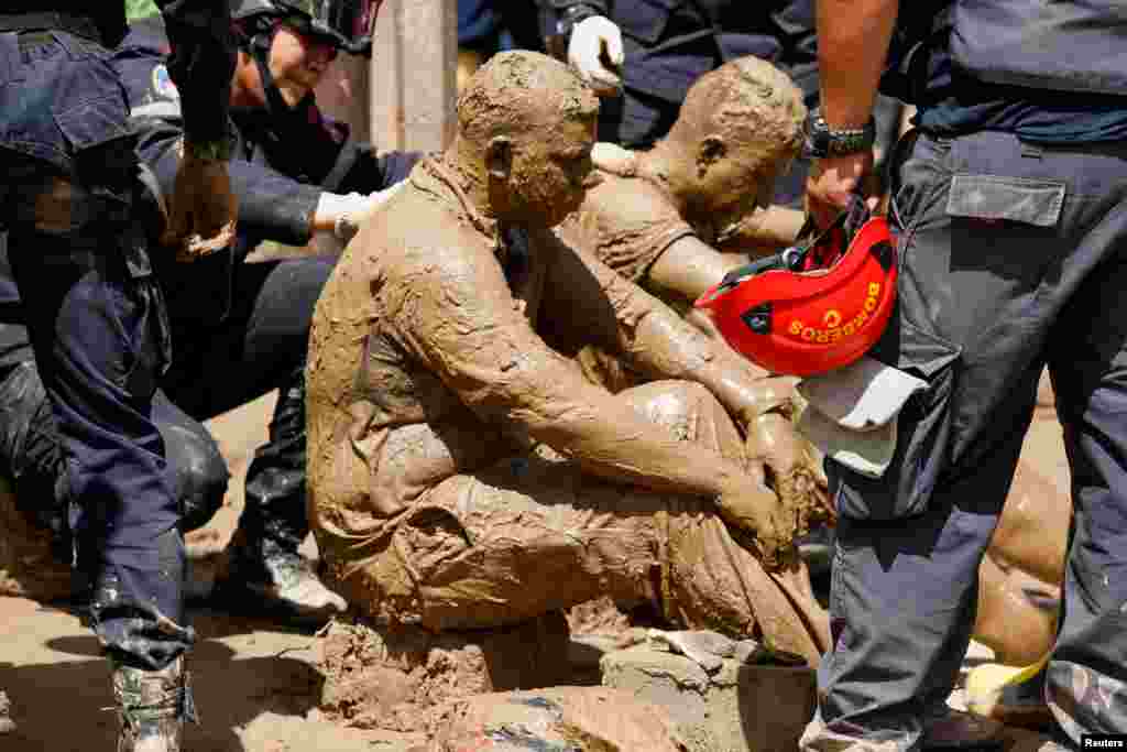 Volunteer rescuers who were attacked by wasps while removing debris to recover the body of a person are attended to by firefighters in Las Tejerias, Aragua state, Venezuela, Oct. 10, 2022. The search continues for missing persons who were swept away Saturday by devastating floods following heavy rain.