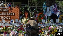 Un agente de policía se agacha frente a un monumento improvisado en la Escuela Primaria Robb en Uvalde, Texas, EEUU, el 29 de mayo de 2022.