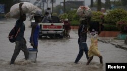 Cuatro personas cruzan una calle inundada durante el paso de la tormenta tropical Laura, en Puerto Príncipe, Haití, el 23 de agosto de 2020.