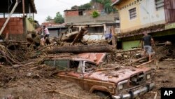 Residents walk through the debris left by flooding caused by a river that overflowed after days of intense rain in Las Tejerias, Venezuela, Oct. 9, 2022.