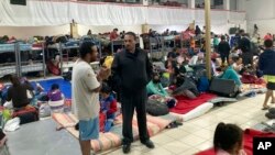 Gustavo Banda (de pie a la derecha), pastor del Templo Embajadores de Jesús, en el albergue para migrantes más grande de Tijuana, México, habla con algunos de ellos el lugar, el 13 de octubre de 2022.