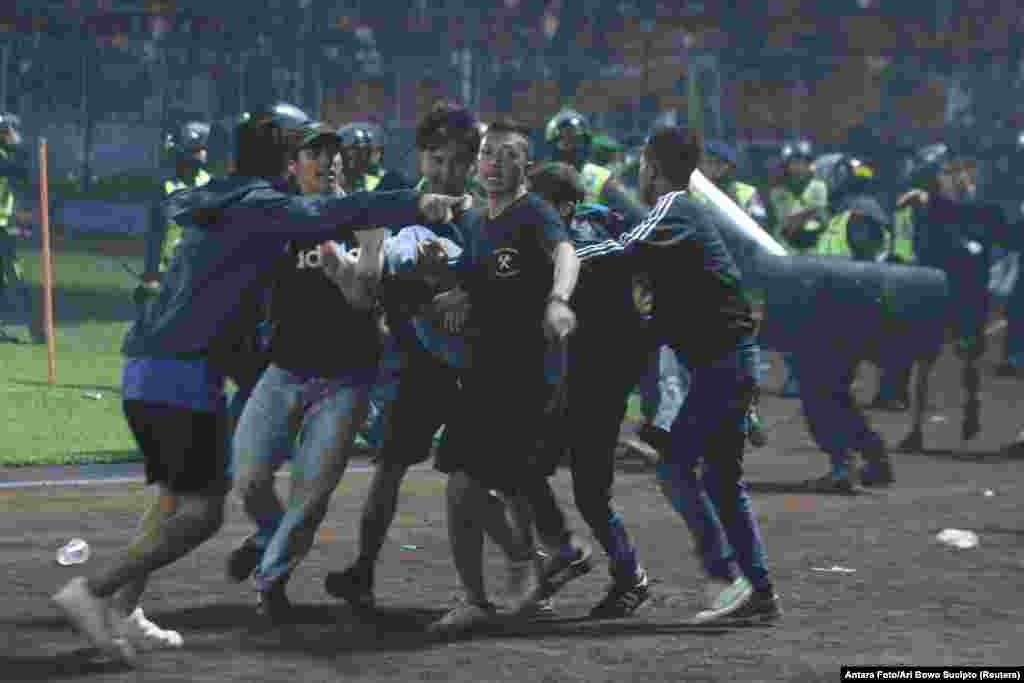 Fans evacuate a man hit by tear gas fired by police during the riot after the league BRI Liga 1 football match between Arema vs Persebaya at Kanjuruhan Stadium, Malang, East Java province, Indonesia.