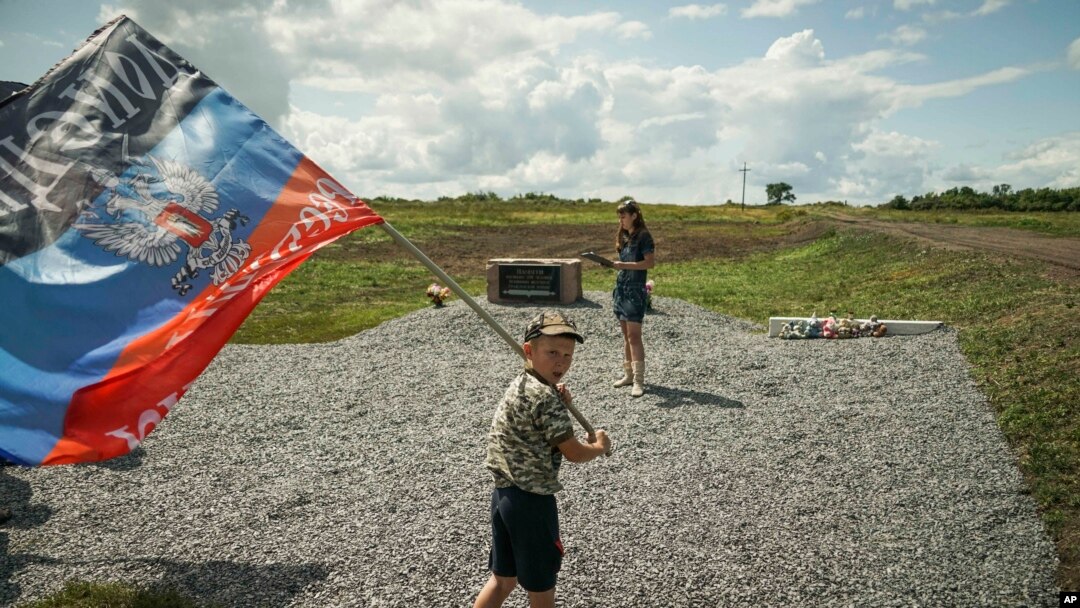 Seorang anak lelaki mengibarkan bendera Republik Rakyat Donetsk, sebuah negara yang diproklamasikan sendiri, di tempat dimana pesawat Malaysian Airlines MH17 ditembak jatuh di desa Hrabove, sebelah timur Ukraina, Kamis, 16 Juli 2015 (foto: AP Photo/Mstyslav Chernov)