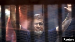 Mantan Presiden Mesir Mohamed Mursi melambaikan tangan saat memasuki ruang sidang bersama anggota Ikhwanul Muslimin lainnya di Kairo, 16 Mei 2015 (Foto: dok). 