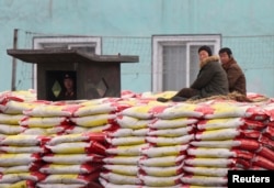 FILE - People sit on sacks of fertilizers as a North Korean soldier stands guard on the banks of Yalu River near the North Korean town of Sinuiju, opposite the Chinese border city of Dandong, Jan. 29, 2014.