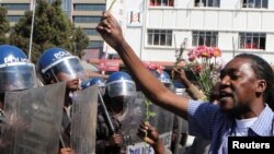 Des manifestants tenant des fleurs dans ses mains pour symboliser la paix, font face à la police anti-émeute à Harare, Zimbabwe, 17 août 2016.