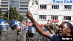 Un policier anti-émeute regarde un manifestant tenant des fleurs pour symboliser la paix à Harare, Zimbabwe, le 17 août 2016.
