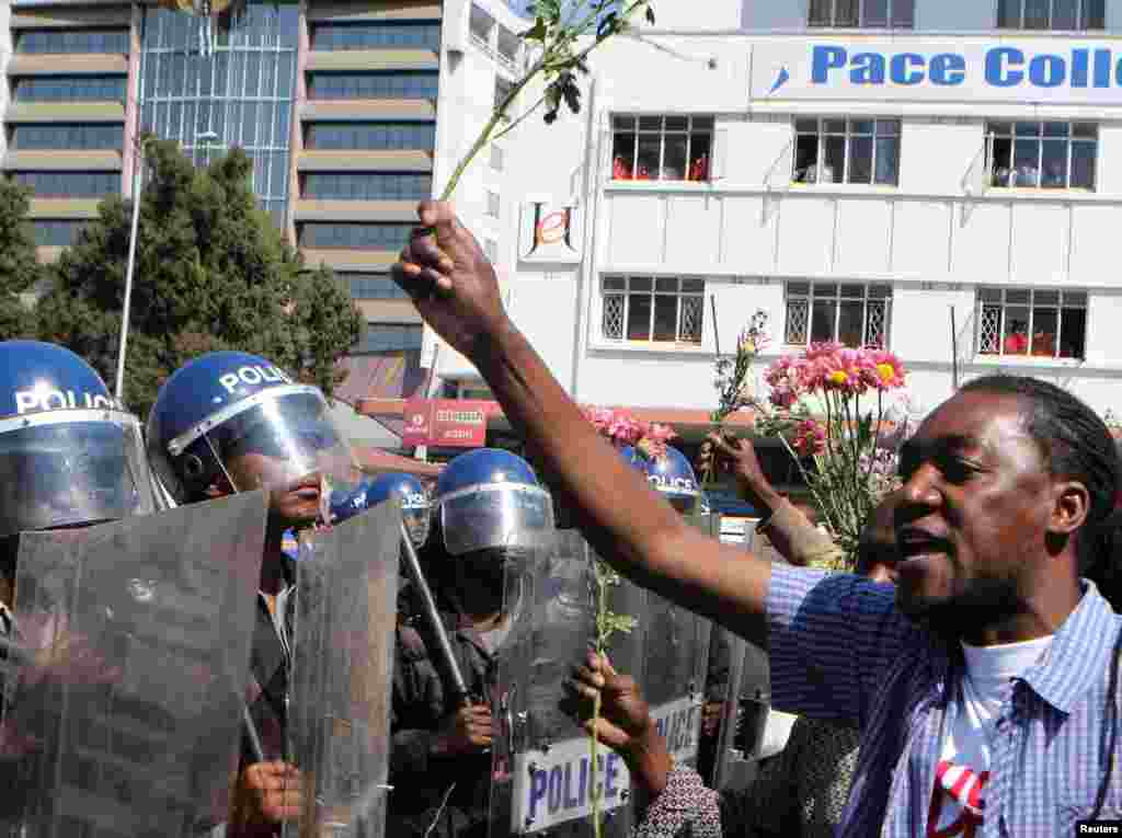 Un policier anti-émeute regarde un manifestant tenant des fleurs dans ses mains pour symboliser la paix à Harare, Zimbabwe, le 17 août 2016.