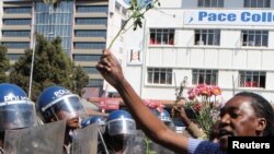 Un policier anti-émeute regarde un manifestant tenant des fleurs dans ses mains pour symboliser la paix à Harare, Zimbabwe, le 17 août 2016.