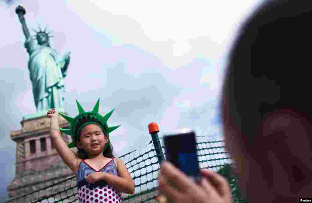 Seorang gadis cilik berpose untuk foto saat berkunjung ke Patung Liberty dan Pulau Liberty yang baru dibuka untuk publik pada 4 Juli setelah ditutup karena Badai Sandy.