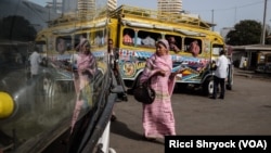 A pedestrian passes a colorful car rapide, with her image reflected in the windshield of a modern Chinese brand King Long bus. Authorities plan to phase out cars rapide by late 2018. (R. Shryock/VOA)