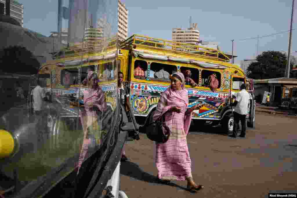 A pedestrian passes a colorful car rapide, with her image reflected in the windshield of a modern Chinese brand King Long bus. Authorities plan to phase out cars rapide by late 2018.