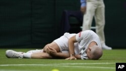 Adrian Mannarino of France lies on the ground in pain during the men's singles first round match against Switzerland's Roger Federer on day two of the Wimbledon Tennis Championships in London, Tuesday June 29, 2021. (AP Photo/Kirsty Wigglesworth)