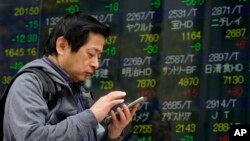 A man uses smartphone in front of an electronic stock indicator of a securities firm in Tokyo, March 26, 2018.