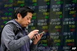FILE - A man uses smartphone in front of an electronic stock indicator of a securities firm in Tokyo, March 26, 2018.