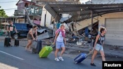 Foreign tourists pull their suitcases as they walk past damaged buildings following a strong earthquake in Pemenang, North Lombok, Indonesia August 6, 2018 in this photo taken by Antara Foto. Antara Foto/Ahmad Subaidi/ via REUTERS