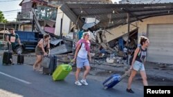 Beberapa turis asing membawa barang-barang mereka melewati kawasan yang hancur akibat gempa di Lombok, hari Senin (6/8).