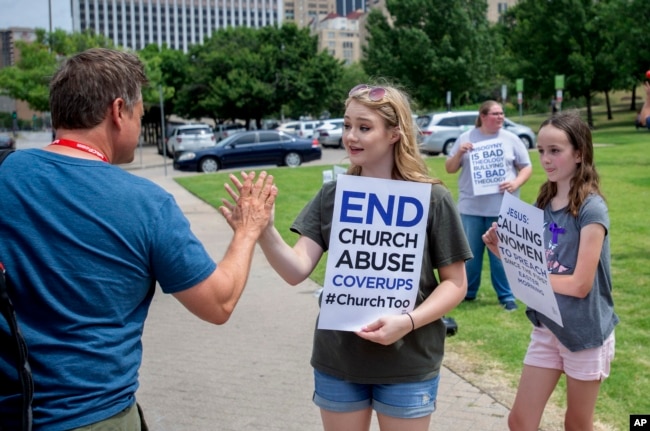 FILE - Claire Summers, 16, gets a high five as she and her sister Ella Summers, 10, right, protest the Southern Baptist Convention's treatment of women outside the convention's annual meeting at the Kay Bailey Hutchison Convention Center in Dallas, June 12, 2018.