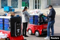 FILE - People retrieve their parcels from a JD.com driverless delivery robot in Tianjin, China, Nov. 12, 2018.
