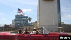 FILE - Tourists ride in a vintage car in front of the U.S. Embassy in Havana, Cuba, March 17, 2016.