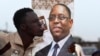 FILE - A man sticks out his tongue next to an election poster of incumbent Senegalese President Macky Sall in Pikine, Senegal, Feb. 7, 2019.