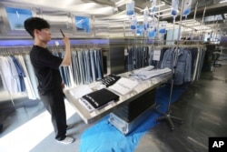 In this May 24, 2019, photo, customer Kim Kun Woo uses his smartphone to take photos at an unmanned jeans shop in Seoul, South Korea. The 24/7 denim shop lets customers try on jeans and pay using a self-service digital system.