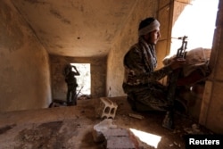 FILE - Kurdish People's Protection Units (YPG) fighters take up positions inside a damaged building in al-Vilat al-Homor neighborhood in Hasaka city, Syria.