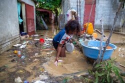Yoleine Toussaint, 22, removes mud from plates in front of her flooded house, one day after the passing of Tropical Storm Laura, in Port-au-Prince, Haiti, Aug. 24, 2020.