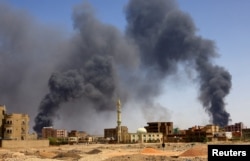 FILE - A man walks as smoke rises above buildings after an airstrike in Khartoum, Sudan, May 1, 2023, two weeks after the Sudanese National Army began fighting the rival Rapid Support Forces militia.