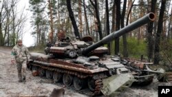 Një ushtar ukrainas ecën përreth një tanku të shkatërruar rus