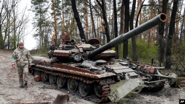 Një ushtar ukrainas ecën përreth një tanku të shkatërruar rus