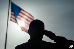 FILE - In this photo taken Aug. 26, 2019 and released by the U.S. Air Force, a U.S. Air Force Staff Sgt., salutes the flag during a ceremony signifying the change from tactical to enduring operations at Camp Simba, Manda Bay, Kenya.