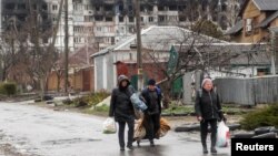 Local residents walk in front of a residential building damaged in the course of the Ukraine-Russia conflict, in the southeastern port city of Mariupol, Ukraine, April 13, 2022. 