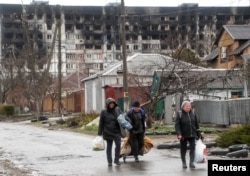 Local residents walk in front of a residential building damaged in the course of Ukraine-Russia conflict, in the southern port city of Mariupol, Ukraine, April 13, 2022.