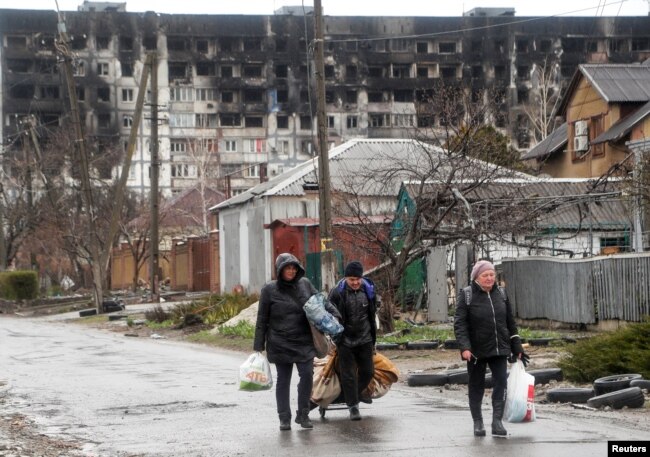 Warga berjalan di depan bangunan tempat tinggal yang rusak akibat konflik Ukraina-Rusia, di selatan kota pelabuhan Mariupol, Ukraina, 13 April 2022. (Foto: Reuters)