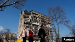 Sejumlah warga berjalan melintas di depan apartemen di Mariupol, Ukraina yang rusak saat penyerangan Rusia ke Ukraina, 15 April 2022. (Foto:Alexander Ermochenko/Reuters)