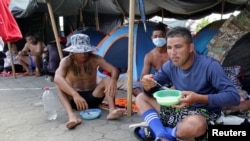 Migrantes cubanos comen en un campamento, instalado por cubanos varados en South Drain mientras esperan el servicio de ferry de Surinam a Guyana, mientras intentan llegar a Estados Unidos, en Nickerie, Surinam, el 11 de diciembre de 2020.