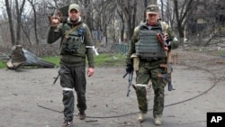 Armed militia members of the self-proclaimed Donetsk People's Republic look at a photographer as they carry captured weapons in an area controlled by Russian-backed separatist forces in Mariupol, Ukraine, April 15, 2022. 