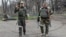 Armed militia members of the self-proclaimed Donetsk People's Republic look at a photographer as they carry captured weapons in an area controlled by Russian-backed separatist forces in Mariupol, Ukraine, April 15, 2022. 