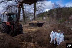 An excavator lifts a casket from a mass grave as volunteers look on, during an exhumation of four civilians killed, in Mykulychi, Ukraine, April 17, 2022.