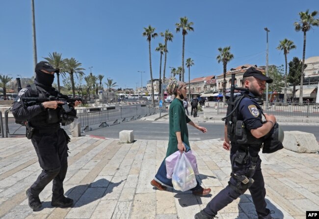 Anggota polisi perbatasan Israel mengawal seorang perempuan Israel di dekat Gerbang Damaskus di Kota Tua Yerusalem, di tengah langkah-langkah keamanan yang meningkat, 15 April 2022. Lebih dari 100 orang terluka dalam kekerasan baru, yang terjadi setelah tiga minggu ketegangan akibat kekerasan di Israel dan Tepi Barat bersamaan dengan perayaan Passover warga Yahudi, Paskah umat Kristiani dan bulan suci Ramadan umat Muslim. (Foto: GIL COHEN-MAGEN / AFP)