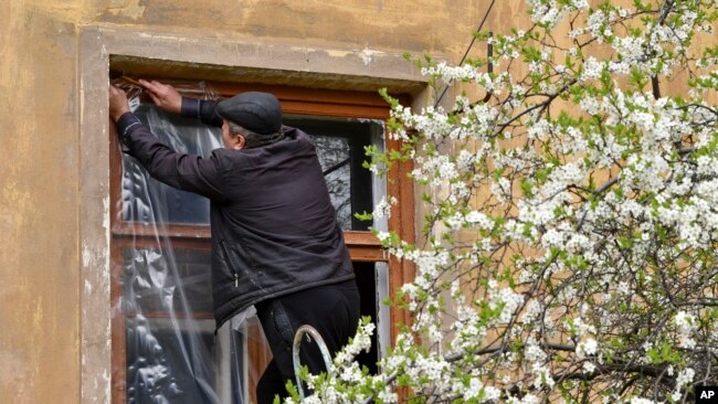 A man puts plastic covers on a window of an apartment building following night shelling in Kramatorsk, Ukraine, Monday, April 18, 2022.