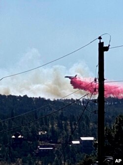 This photo provided by the Village of Ruidoso shows a fire fighting air tanker dropping fire retardant across the mountains near the Village of Ruidoso, N.M., April 13, 2022.
